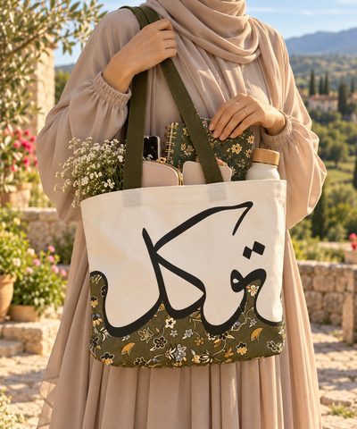 Muslim woman wearing a taupe hijab carrying a Makkah Arabic calligraphy canvas tote bag over her shoulder in a peaceful countryside setting.